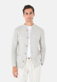 Cardigan lavorato a maglia grigio chiaro con scollo rotondo, quattro bottoni di legno, due tasche frontali e texture a coste. Indossato sopra una camicia bianca.