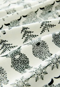 Baumwollstoff mit einem schwarz-weißen Muster, das stilisierte Schafe und Schneeflocken auf einem cremefarbenen Hintergrund zeigt, mit weicher Textur und glatten Falten.