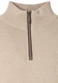 Beige gerippter Strickpullover mit hohem Kragen und einem silbernen Metall-Quarter-Zipper in der Mitte vorne.