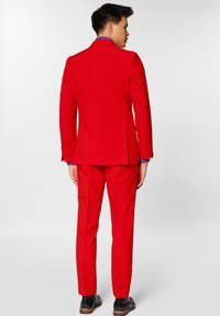 Crveni odijelo sa slim fit sakoom i hlačama. Glatka tkanina, s jednim prorezom na leđima, uparen s crnim cipelama i plavom košuljom ispod.
