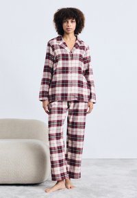 Rute pyjamasæt i røde og creme farver, der indeholder en knaplukket top med krave og lange ærmer, parret med matchende lige bukser.
