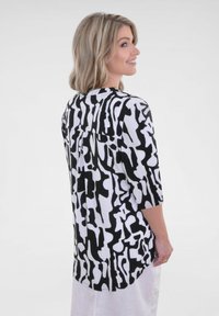 Blouse à motifs noir et blanc avec des manches trois-quarts, encolure ronde et coupe ample, dotée d'un ourlet courbé et d'une texture subtile.