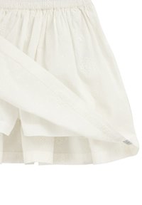 Gonna bianca con vita elastica e ricamo floreale a occhiello, che mostra la fodera interna e i dettagli del tessuto.