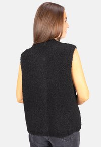 Schwarze ärmellose Weste aus strukturiertem Stoff mit einem samtigen Finish. Sie hat einen hohen Halsausschnitt und eine lockere Passform, mit sichtbaren Nähten.
