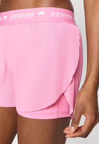 Ροζ πλισέ σορτς με λογότυπο VENUM στη μέση. Το ύφασμα φαίνεται ελαφρύ με απαλή υφή και πολυεπίπεδο σχέδιο.