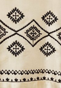 Beige fabric with black embroidered patterns including diamond and floral motifs. Features intricate detailing and decorative borders.