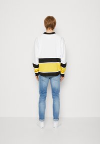 Felpa bianca oversize con righe orizzontali nere e gialle, abbinata a jeans blue chiaro e sneakers bianche.