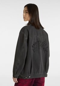 Oversized zwarte denimjas met een gestructureerd grafisch ontwerp op de achterkant, drukknoopsluiting op de taille en een klassieke kraag.