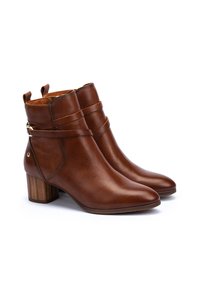 Brown leather ankle boots with a pointed toe, a block heel, and decorative straps around the ankle. Textured back panel and gold hardware accent.