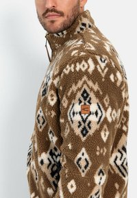 Brauner Fleece-Pullover mit creme- und schwarzen geometrischen Mustern. Verfügt über einen hohen Kragen und ein Lederakzentpatch am linken Ärmel.