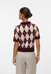 Polo en tricot à manches courtes, marron avec un motif de losanges roses et crème. Doté d'un col plat et d'un ourlet côtelé. Texture lisse, coupe moderne.