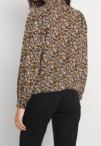Blusa nera a fiori con maniche lunghe, caratterizzata da un collo alto e una schiena con apertura a goccia. Piccole fantasie floreali multicolori su uno sfondo scuro.