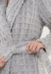 Bata de baño de felpa gris con un patrón de cuadros texturizado. Presenta un cinturón a la cintura y un amplio cuello. El material suave y aterciopelado aumenta la comodidad.