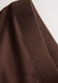 Nahaufnahme eines braunen Stoffes mit sichtbaren geraden Nähten entlang der Naht auf hellem Hintergrund.