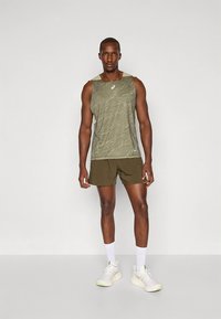 Canotta leggera verde oliva con motivo a rilievo, abbinata a pantaloncini verde oliva scuro. Il modello indossa calzini bianchi e scarpe da ginnastica.