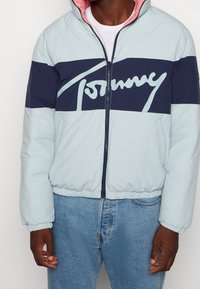 Světle modrá péřová bunda s námořnickou horizontální pruhovanou částí, velkým bílým logem "Tommy", růžovým vnitřním límcem a elastickými manžetami a spodním lemem.