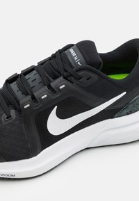 Black athletic shoe with mesh upper, white Nike swoosh, and green lining. Features prominent lacing and textured black accents.