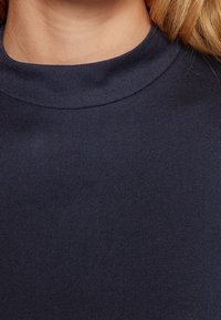 Marinblå höghalsskjorta med en slät, solid textur, som har en svängd halsringning och inga synliga mönster eller dekorationer.