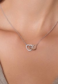 Srebrny naszyjnik z połączonymi kształtami serca i litery B, ozdobiony małymi przezroczystymi cyrkoniami na delikatnym łańcuszku.