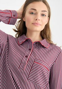 Camicia a righe rossa e bianca con colletto, polsini con dettagli a bottoni e una tasca sul petto con un motivo a righe abbinato.