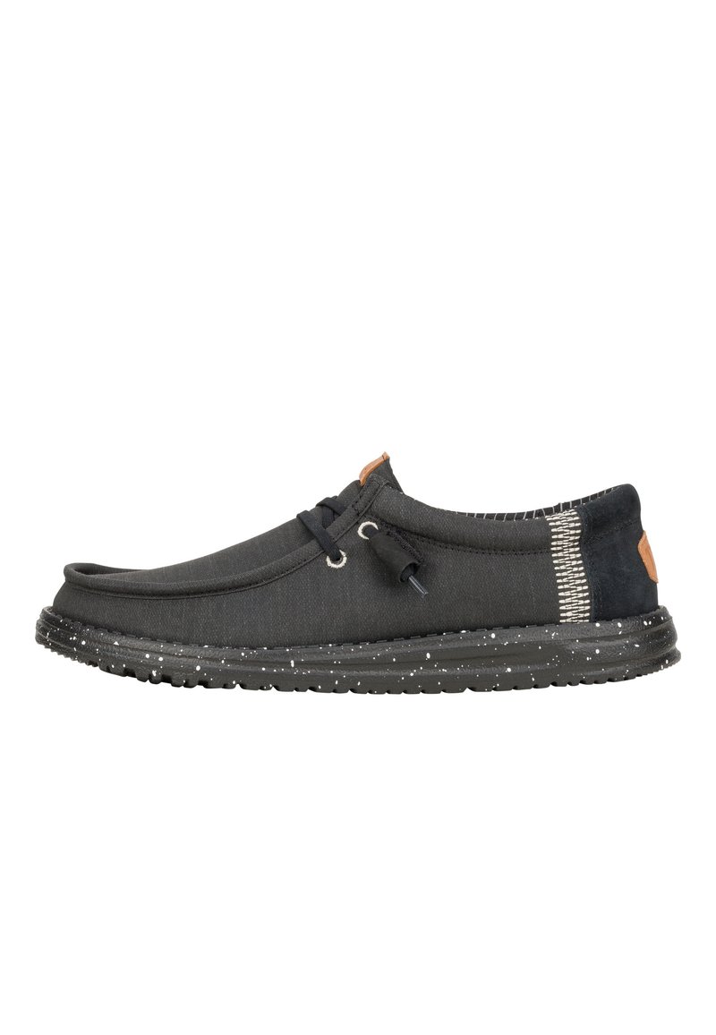 Zapato de lona negro sin cordones con punta redonda, acentos laterales grises texturizados, suela blanca salpicada y detalles de cuero de contraste en el talón.