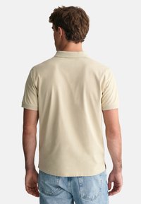 Beige kortärmad pikétröja med mjuk textur, klassisk krage och avslappnad passform. Bärs med ljusblå denimjeans.