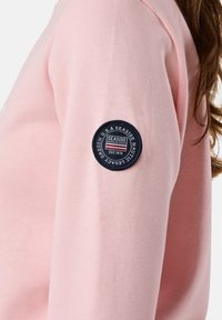 Felpa rosa con una texture morbida, caratterizzata da un distintivo circolare blu navy sul maniche che riporta la scritta "Seaside Nautical Legacy Est. 1976."