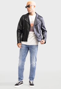 Sort faux læder bikerjakke med sølv lynlåse, båret over en lys skjorte med vandrette striber, parret med blå jeans og sorte sneakers.