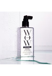 Flacone spray del trattamento per capelli WOW Color Wow Extra Strength Dream Coat con gocce d'acqua sulla bottiglia e sulla superficie.