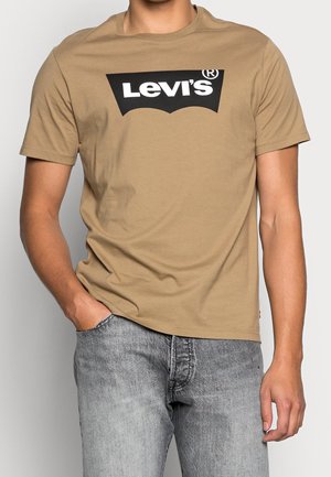 Brun bomulds t-shirt med et stort sort Levi's logo over brystet. Kombineret med lysegrå denimjeans. Kortærmet og løs pasform.
