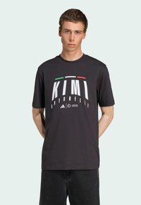 Sort bomulds T-shirt med stor hvid tekst "KIMI ANTONELLI" med italienske flagfarver ovenover. Rund hals, korte ærmer, afslappet pasform.