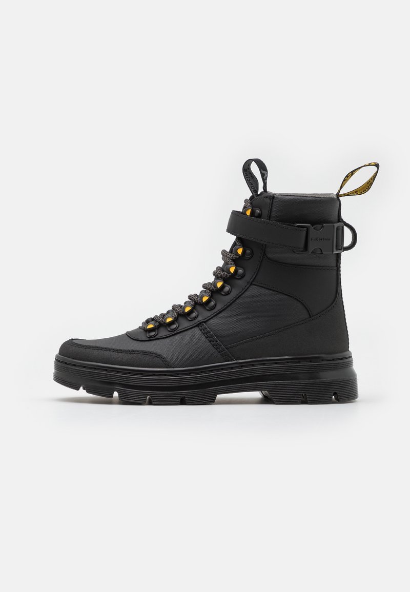 Botte noire montante avec semelle épaisse, œillets avec accent jaune, laçage à l'avant, sangle réglable et languettes d'extraction à la cheville et au talon.