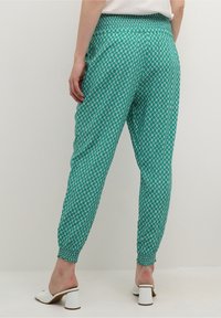 Turkosa mönstrade joggers med elastiskt midjeband och muddar. Har en geometrisk design i ljusgrön och krämfärgad. Kompletteras av vita klackskor.