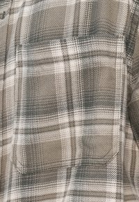 Koszula w kratę w odcieniach szarości i beżu, wykonana z teksturowanej tkaniny, z kieszenią na piersi i standardowym kołnierzykiem.