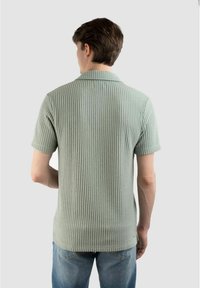 Ljusgrön ribbad polo med texturerad tyg, har klassisk krage och korta ärmar, bärs tillsammans med avslappnade blå jeans.