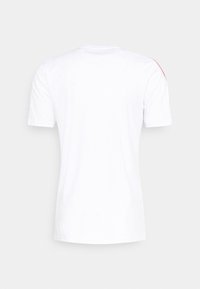 Vit kortärmad t-shirt i bomull, med rund halsringning och en kontrasterande röd detalj på axeln. Slät textur.