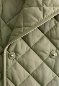 Quilted outerwear in olive green fabric, featuring diamond patterns, contrasting stitching, and metal snap buttons for closure. Soft texture.