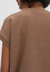 Top marrone a maniche corte con superficie texturizzata caratterizzata da sottili linee verticali. Collo semplice. Nessun elemento decorativo o abbellimento visibile.