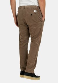 Brown corduroy pants with a relaxed fit, featuring two back pockets and a woven label. The material has a soft texture and visible ribbing.