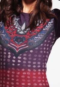 Paarse en rode gestreepte textieltop met een grafisch ontwerp van stippen en kronkels, waarbij een mix van gladde en gestructureerde afwerkingen wordt benadrukt.