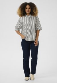 Camicia a righe bianca e nera con maniche corte, abbinata a jeans blu scuro e scarpe chiare.