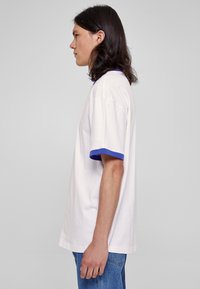 Hvit t-skjorte med blå ribbet krage og mansjetter, løs passform, korte ermer og klassisk rund hals, sammen med blå denim jeans.