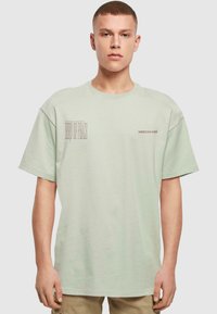 Light green oversized t-shirt in cotton fabric with short sleeves. Features printed text on the front and a relaxed fit.