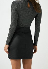 Mini jupe en faux cuir noir associée à un haut ajusté à manches longues scintillant avec un détail en forme de trou de serrure au dos.