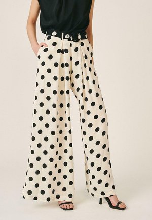 Pantalones de pernera ancha color crema con grandes lunares negros, cintura alta, cinturón a juego, combinados con top negro y tacones negros abiertos.