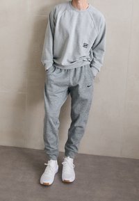 Grauer Pullover mit gerippten Bündchen und Kragen, kombiniert mit passenden grauen Jogginghosen mit einem schwarzen Nike-Logo und weißen Schuhen mit Gummisohlenakzenten.