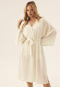 Kremowy kimono z lekkiego materiału, z zapinaniem na krzyż, szerokimi rękawami i wiązaniem w pasie.