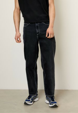 Schwarze Jeans aus Denim mit geradem Schnitt, hervorgehoben durch kontrastierende Nähte, im Fünf-Taschen-Design und einem klassischen Reißverschluss. Kombiniert mit Sportschuhen.