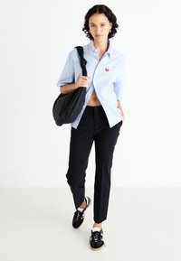 Light blue short-sleeve button-up shirt with a small red heart detail, black fitted pants, and black sneakers with white accents and textured surface.