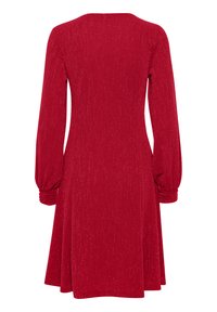 Röd klänning i ett texturerat tyg med långa, sammangruppade ärmar, rundad halsringning och utsvängd kjol, med subtila glittrande detaljer.